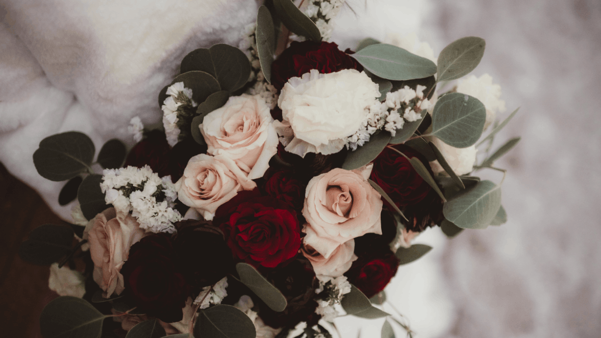 Nahaufnahme eines Brautstraußes aus dunkelroten, blush-farbenen und cremeweißen Rosen mit Eukalyptus.
