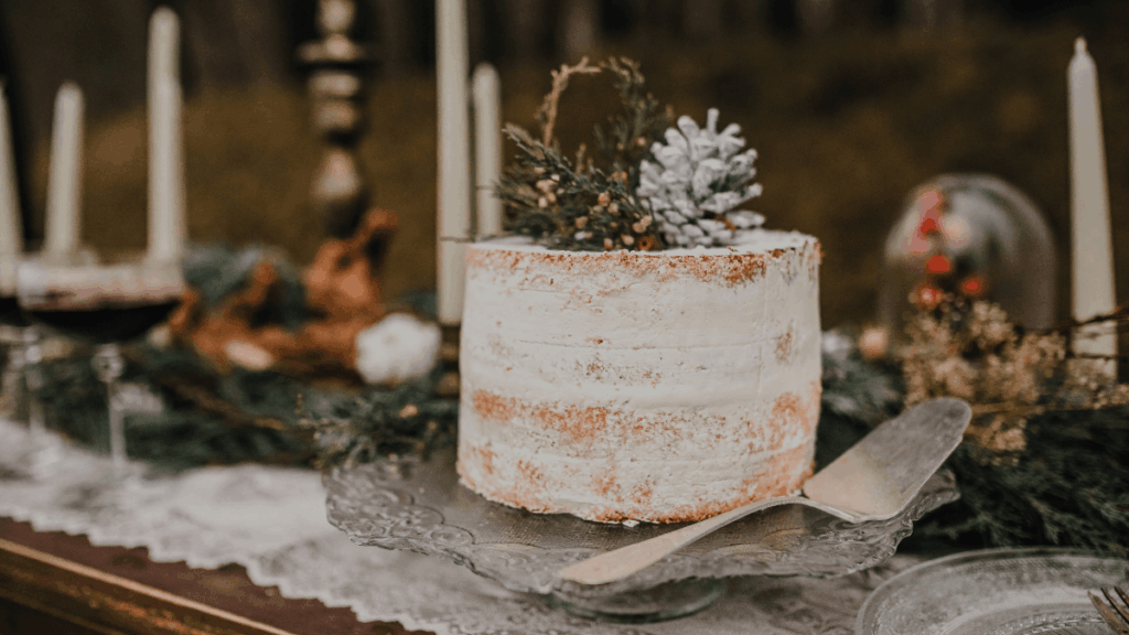 Nahaufnahme einer Naked Cake mit Tannengrün-Topping, umgeben von Kerzen, Leuchtern und winterlicher Tischdekoration.