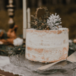 Nahaufnahme einer Naked Cake mit Tannengrün-Topping, umgeben von Kerzen, Leuchtern und winterlicher Tischdekoration.